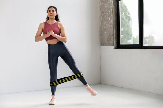 Woman doing a standing banded hip abduction with a loop resistance band around her lower legs, training hip stability and glute strength to reduce “tight” hips from guarding.