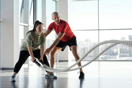 woman pushing through battle rope workout under trainer supervision—activating collagen through intense, load-bearing movement at the gym