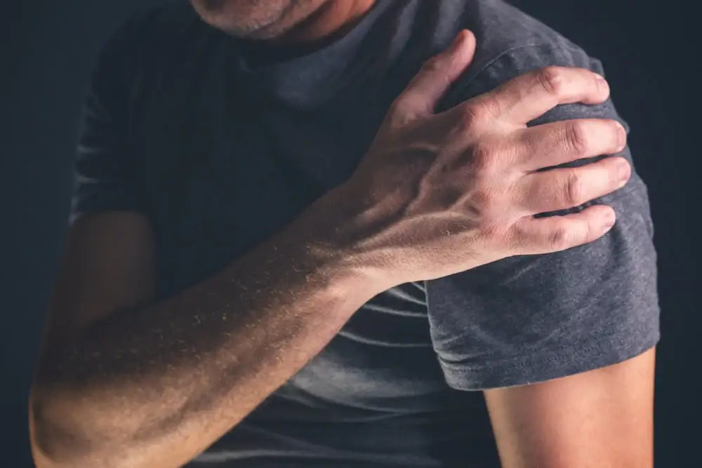 Man holding his shoulder in visible discomfort, reflecting symptoms of rotator cuff strain or irritation commonly caused by poor posture, overuse, or muscle imbalance.