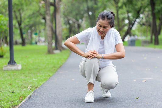 Woman kneeling outdoors, holding her knee in pain after walking, illustrating how pain is a signal to adjust movement, not a reason to stop progressing.