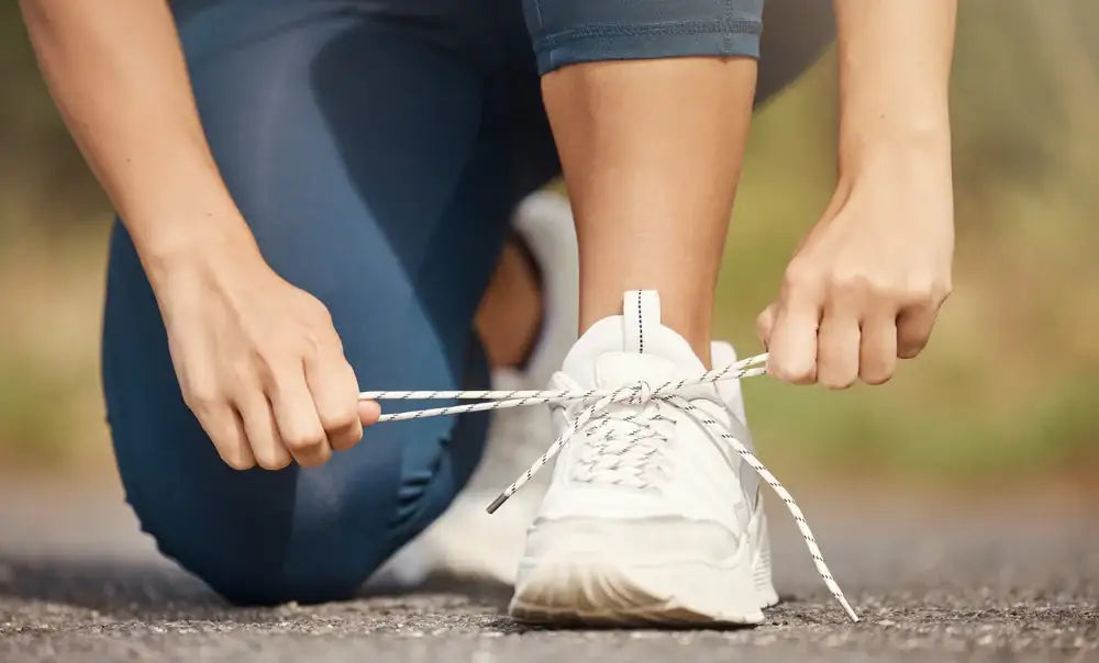 Woman tying running shoes before a walk, symbolizing the power of simple daily movement for long-term fitness, joint health, and consistent energy.