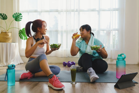 Two friends eating salads together in a home gym after a workout, emphasizing post–exercise nutrition and blood sugar management.