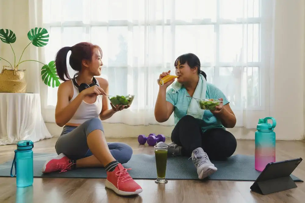 Two friends eating salads together in a home gym after a workout, emphasizing post–exercise nutrition and blood sugar management.