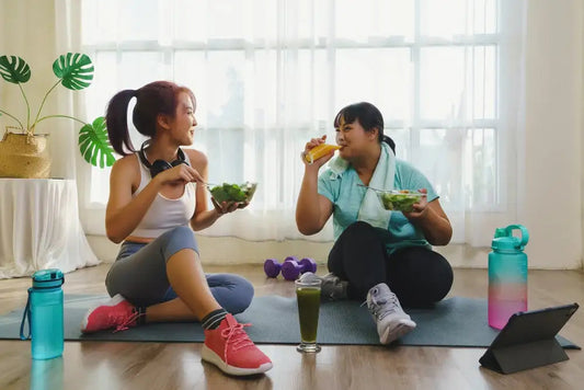 Two friends eating salads together in a home gym after a workout, emphasizing post–exercise nutrition and blood sugar management.