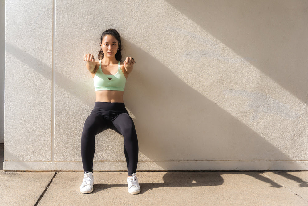 Woman holding a wall sit to build knee stability through isometric training and muscular control.