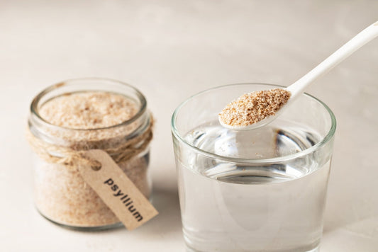 Spoonful of psyllium husk powder being added to a glass of water, illustrating how hydration activates fiber for effective digestion and gut health.