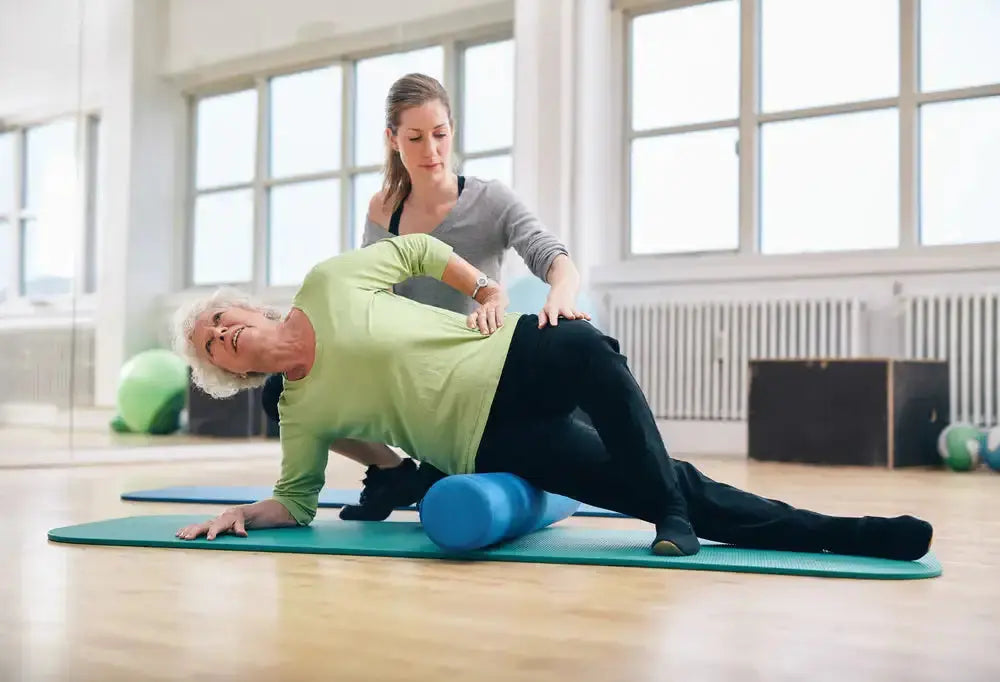 Therapist assists older woman foam rolling her hip, underscoring how short-term relief without core stability keeps the cycle of tightness in motion.