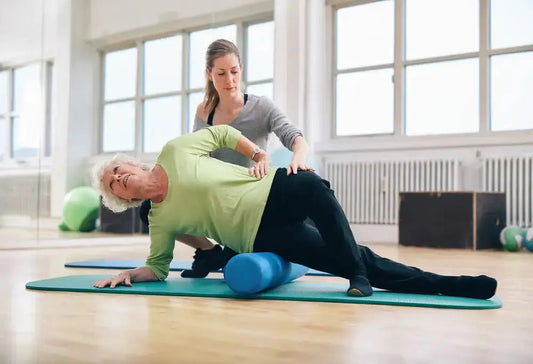 Therapist assists older woman foam rolling her hip, underscoring how short-term relief without core stability keeps the cycle of tightness in motion.