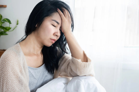 Tired woman sitting up in bed with hand on face, showing signs of poor sleep potentially linked to EMF exposure in the bedroom