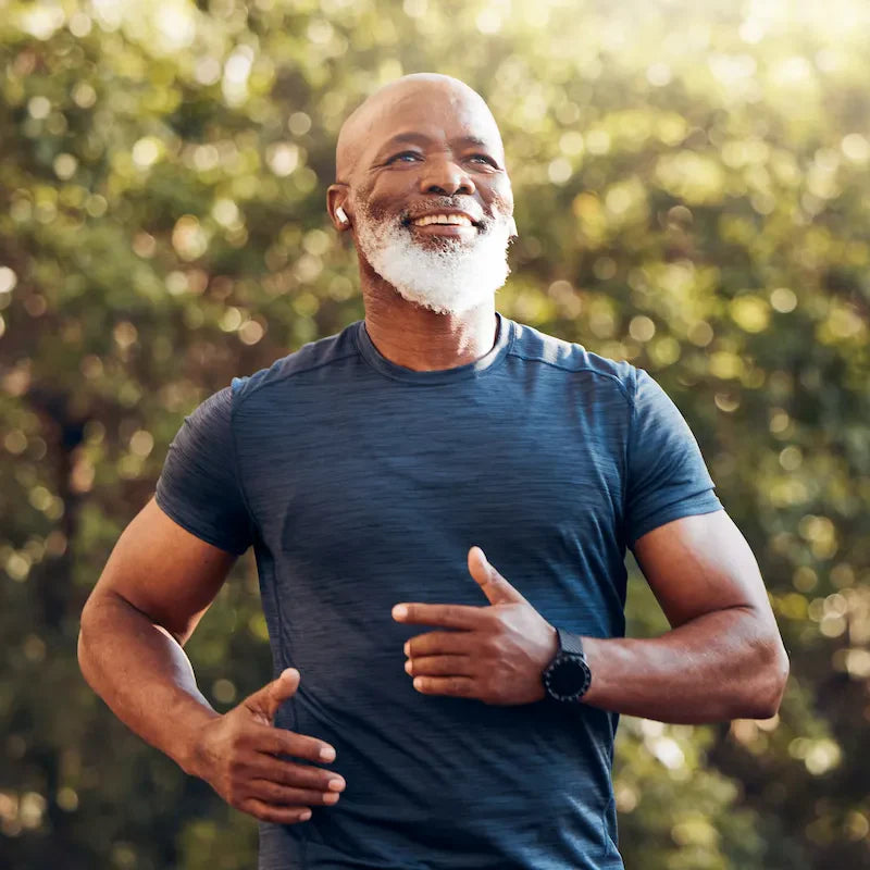 Older man smiling while running outdoors wearing a fitness tracker, representing active healthy aging