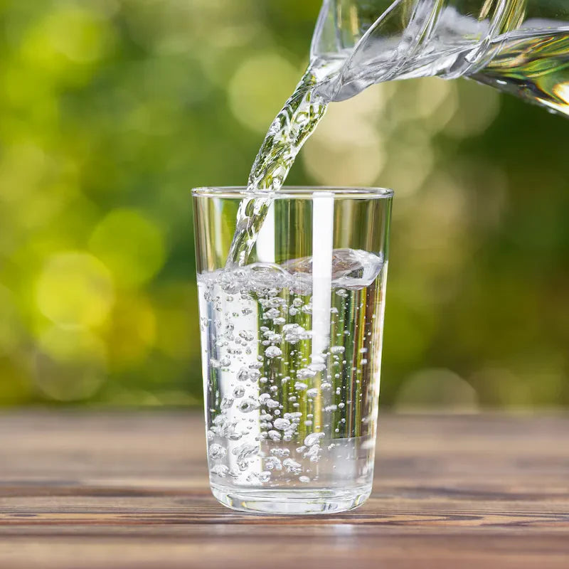 Clear water pouring into a glass against a green natural background, representing daily hydration