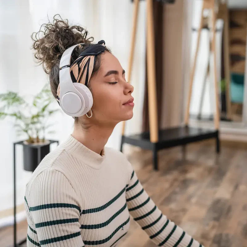 Woman sitting with eyes closed wearing headphones, practicing mindfulness and meditation at home