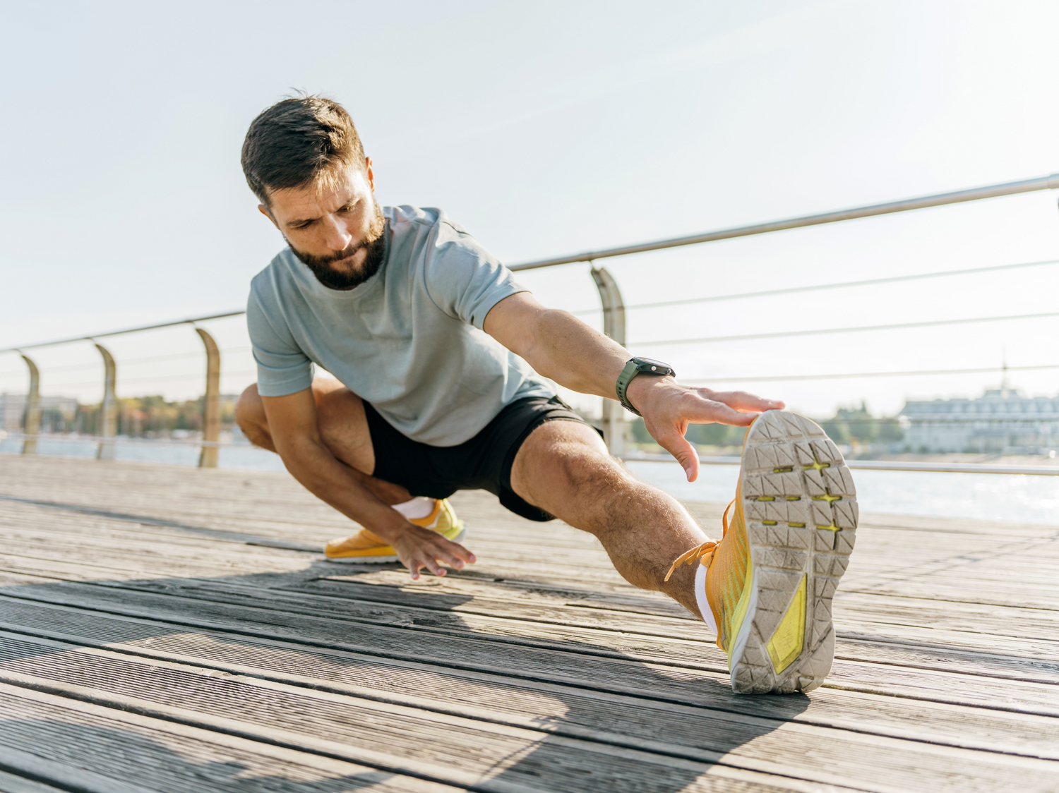 A middle-aged man in athletic wear stretching his leg with focus, surrounded by a tranquil and scenic outdoor setting.