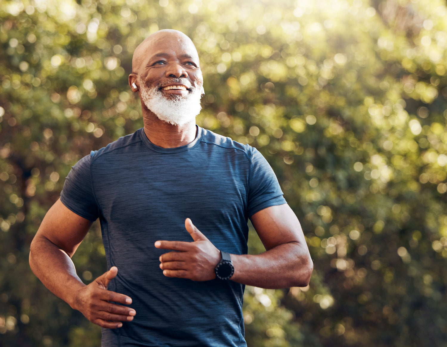 Cheerful senior jogging outdoors on a sunny day, wearing a fitted crew tee, smartwatch, bluetooth earbuds, and a big smile, exuding energy and enthusiasm for fitness and healthy living.