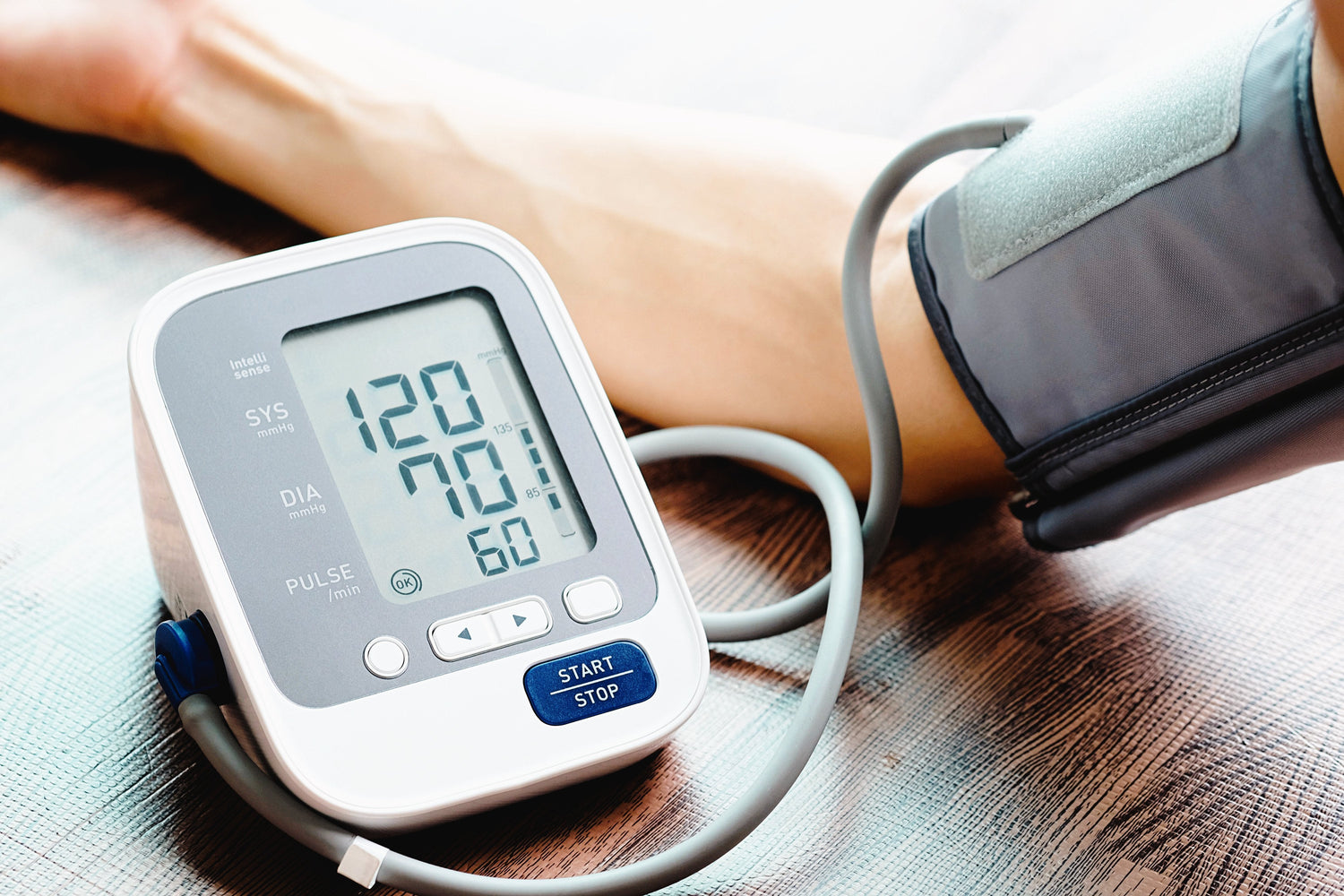 A close-up of a man's arm inserted into a blood pressure cuff, the device wrapped securely around the upper arm, showing a normal reading on a digital monitor in a clinical or home setting.